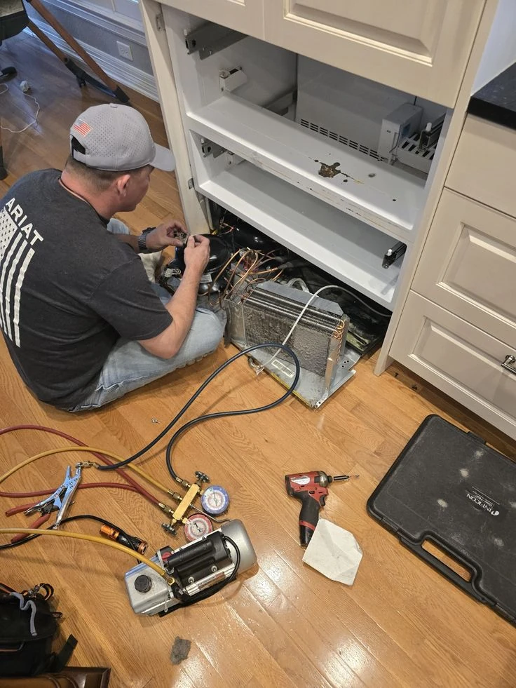 Technician servicing exposed cooling-system components next to kitchen cabinetry