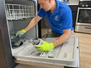 Technician inspecting a removed dishwasher component while wearing protective gloves