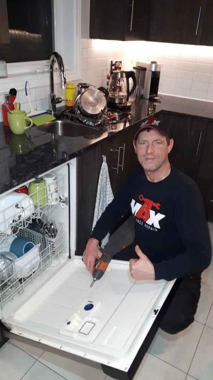 Appliance technician kneeling beside an open dishwasher during a service visit