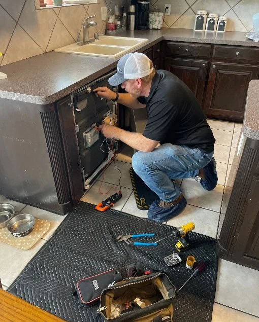 Technician working on a kitchen appliance with diagnostic tools on a protective mat